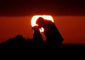 A woman gives her dog a kiss as they watch the sunset at Anchor Bay outside Mellieha