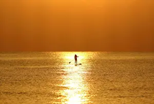 A woman paddles on a stand-up board during sunrise in a beach in Larnaca