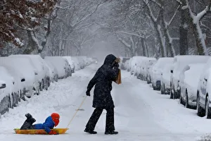 A woman pulls her child on a sled in heavy snow in Brooklyn, New York City