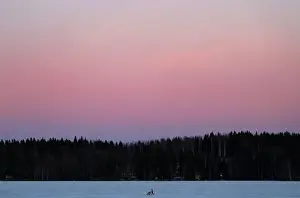 A woman pushes a pram as she walks over a frozen lake during sundown at the Pajulahti