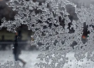 A woman is seen walking in the background through a sheet of glass, on which ice particles A woman is seen walking in the background through a sheet of glass, on which ice particles