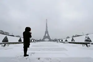 France Prints: A woman takes pictures of the Eiffel Tower in Paris under the falling snow as winter
