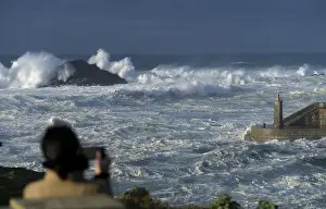 Weather Prints: A woman takes pictures of waves as they crash against a lighthouse in the port town of