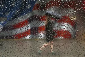 A woman walks with an umbrella in the rain past a U. S. flag painted on a building in